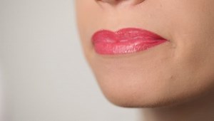 woman smiling and rubbing lips with red lipstick