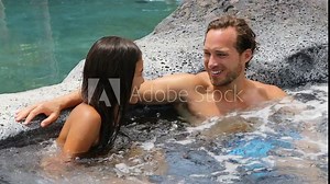 Romantic couple relaxing together in hot tub whirlpool jacuzzi luxury resort spa retreat Luxurious hotel travel vacation. People laughing talking having fun relaxed enjoying summer holidays.