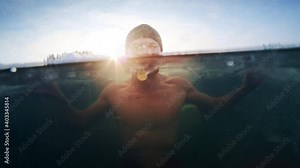Winter swim. Young man swims in the winter lake. Splitted footage with underwater view of the icy water and male in hat bathing among the ice