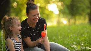 Beautiful mother with her daughter in nature making soap bubbles and laughing