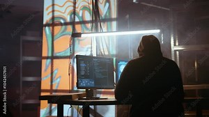Hacker using software interface on computer screen, running programming code in warehouse with graffiti sprayed on walls. Evil developer in underground base building malware, handheld camera shot