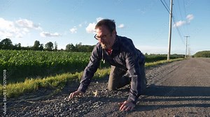 Man on his knees on the side of the road vomiting and looking sick.
