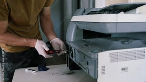 printer repair technician. A male handyman inspects a printer before starting repairs at the service center.