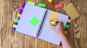 Woman opens notepad and draws smile. Open notepad with office supplies. Open notepad lies on a wooden desktop with marker, pencil, pen and Stickers