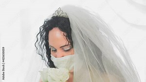 The face of a Jewish bride in a wedding dress and veil in a medical mask in the synagogue hall before the chuppah ceremony with a bouquet of flowers. From blur to sharpness