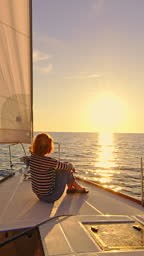 Woman sits on a deck of a sailboat sailing at sunset