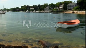 Looking up Pocasset river with orange and white wooden sailboat anchored just off shore. Waterfront property lines the inland shore