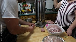 Using stuffer to slowly fill sausage casing with fresh ground marinated pork making wieners or sausages ready to be smoked.