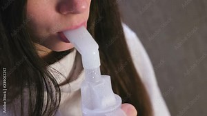 Use nebulizer and inhaler for the treatment. Young woman inhaling through inhaler nozzle for throat sitting on the sofa. Close-up lips and nose.