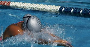 Super slow motion close up of young professional female swimmer with cap and goggles swimming with passion and motivation to achieve a victory in competition while practicing in swimming pool.