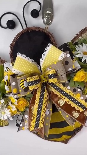 Buzz into summer with this adorable bee-shaped bumblebee wreath for your front door, handcrafted with charming florals, playful bee accents, and a show-stopping bow! Designed on a grapevine frame, this whimsical wreath features a three-dimensional bee body, complete with rustic burlap wings and wired antennas for added personality. Each wing bursts with bright yellow roses, white daisies, blue filler florals, and greenery—bringing your entryway to life with sunny cheer. The layered bow steals th