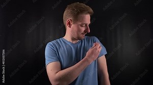 a composed young man administers an injection into his own arm on a black backdrop. The syringe represents medicine, vaccine or managing a condition like diabetes. Medicine, self-care, healthcare