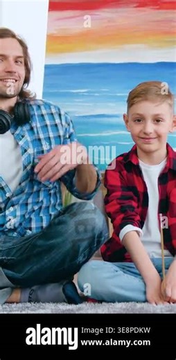 Arts concept where attractive joyful satisfied skilful dad and son posing on camera on fluffy carpet in art home studio during drawing picture on canvas with brushes and acrylic paints Stock Video Footage - Alamy