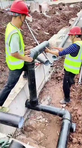 On a muddy construction site, two masters use tools to precisely connect drainage pipes—for detail-