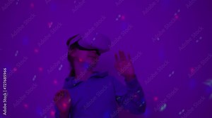 Girl Using Virtual Reality Headset And Looking Around At Interactive Technology With Colorful Illumination. VR Entertainment Immersive. Girl Wearing VR Headset in World of Virtual Reality Interacting.
