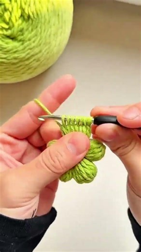 Green yarn loops through crochet hook, textured leaf pattern slowly emerges.