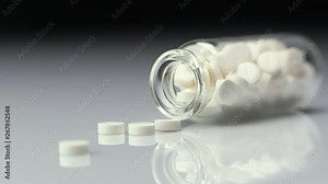 White pills in bottles. Bottle fall over and Pills are falling out from the bottle on the table. Macro closeup slow motion.