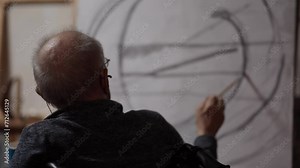 Senior artist on a wheelchair paints an oil painting on canvas in a studio