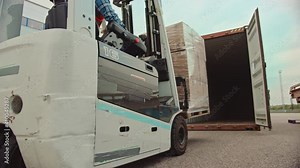 Forklift Driver Loading a Shipping Cargo Container with a Full Pallet with Carboard Boxes in Logistics Operations Port Terminal. Tracking Shot from the Side Shows How Pallet is Brought by the Machine.