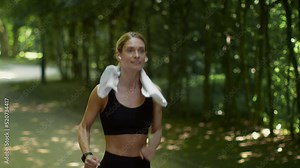 Intensive cardio training. Active middle aged lady jogger running in public park and looking at her smartwatch