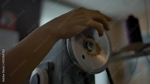 Working on industrial sewing machine. Tailor's graceful hand with manicure spinning balance wheel controlling stitching. Atelier or sewing workshop background. Tailoring clothes process.