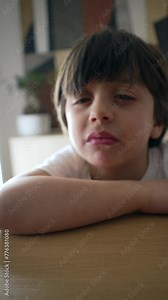 One upset little boy leaning on table with an expression of deception, bored sad 5 year old child, vertical video