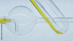 Yellow natural oil flows through laboratory spherical glass tube. Cosmetic natural oil flows through thin curved glass tubes in laboratory. Filtration process of natural essential oils.