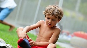 Child removes socks. Candid moment of young boy removing wet socks to play in the lawn