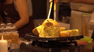 Super slow motion shot A woman is cooking food on a stove. The food is a type of bread. The woman is using tongs to pick up the bread