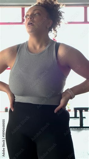 Vertical video: Using battle ropes, woman in grey tank doing waves in gym, checking watch for pulse