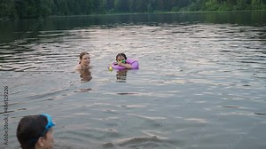 happy children, boy and girl swim in a forest lake. splashing each other. play. enjoying vacations and outdoor recreation. in blue water at sunset; bathe in lake or river and making water drops