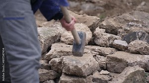 Construction worker breaking rocks with sledgehammer outdoors. A construction worker in blue uniform using a sledgehammer to break rocks on a construction site
