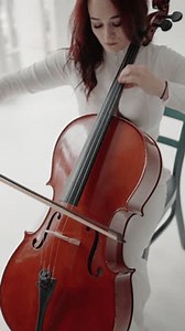A beautiful woman sitting and playing the cello in a studio on a white background. Closeup view of violoncello and hands of musician, A female cellist plays the cello. Vertical video.