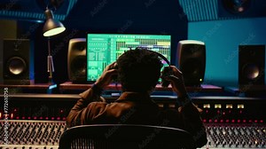 Sound designer editing tracks by adjusting volume levels with panel board knobs and sliders, studio control room. Audio technician mixing and mastering hit song with digital software. Camera B.