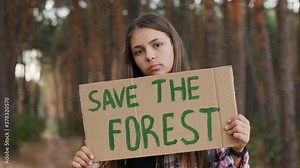 Teenage girl with Save the Forest poster. Young activist holding ecology poster on trees background. Deforestation concept, logging, felled timber in the forest.