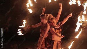 Fire show performance. Three girls female fire performers gather together dancing with burning fire torches shaped as fans on black background. Close-up. Slow motion