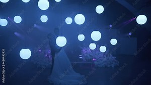 The bride and groom dance the first dance on stage, around them laser projection and many white balls that move up and down