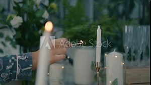 A woman lights candles with a match. Slow motion video recording of a hand holding a lighted match and with it lighting candles placed on the table at home