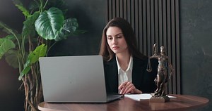 A lawyer or attorney reviews client files, interview transcripts, evidence with a laptop computer in a modern office. Concepts of law and legal services