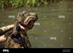 Full military experience - One day commando - running through the water with automatic rifle replica Stock Photo - Alamy