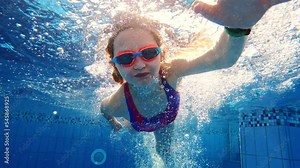 Cute little girl with goggles diving and swimming underwater in a pool