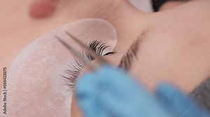 Eyelash extension procedure. The working process of professional beauty master lengthening female lashes. Fake eyelashes. Eyelashes extensions close up. Makeup artist and client in beauty salon.