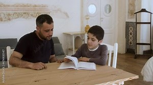 Focused son and father reading book together. Bearded man sitting and explaining homework to boy. Smiling kid turning page on, looking at textbook. Home education, distance learning concept.