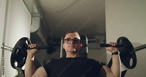 Male client in glasses trains pectoral muscles on the simulator in a gym