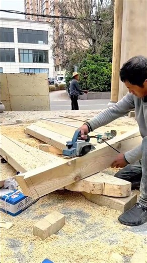 planing the surface of a long wooden beam outdoor using a blue electric handheld power planer tool