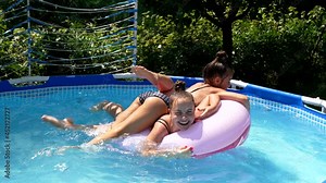 Happy girls have fun floating together on swim ring in outdoor swimming pool, summer
