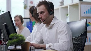 Close up view of angry and nervous call center operator with headset talking with the hotline customer, being irritated, uses bubble wrap to calm down and continues conversation. Stressful situation