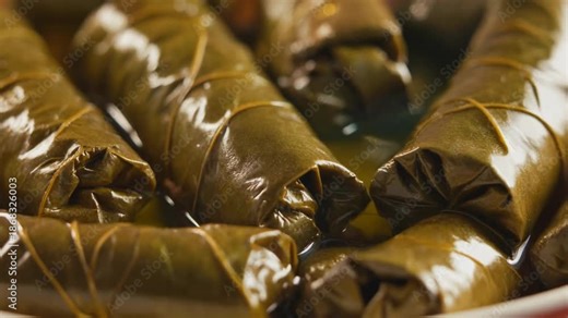Delicious close-up of traditional stuffed grape leaves (dolmades or sarma) simmering in olive oil and broth.