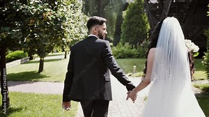 The bride and groom hold hands and walk together. rear view. Slow motion
