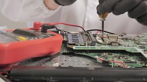 Technician Repairing Motherboard with Tools and Multimeter, Close-up of hands fixing circuit board using screwdriver and diagnostic device in lab coat